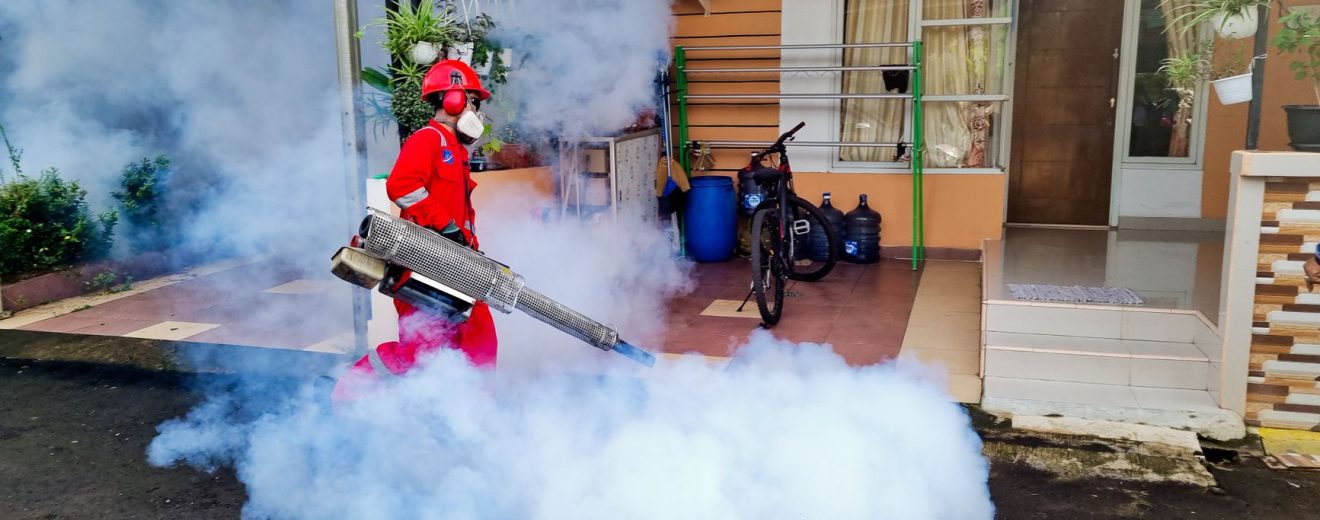 Profissional de controle de pragas utiliza uma máquina de fumaça para fumigar a área externa de uma residência.