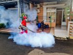 Profissional de controle de pragas utiliza uma máquina de fumaça para fumigar a área externa de uma residência.